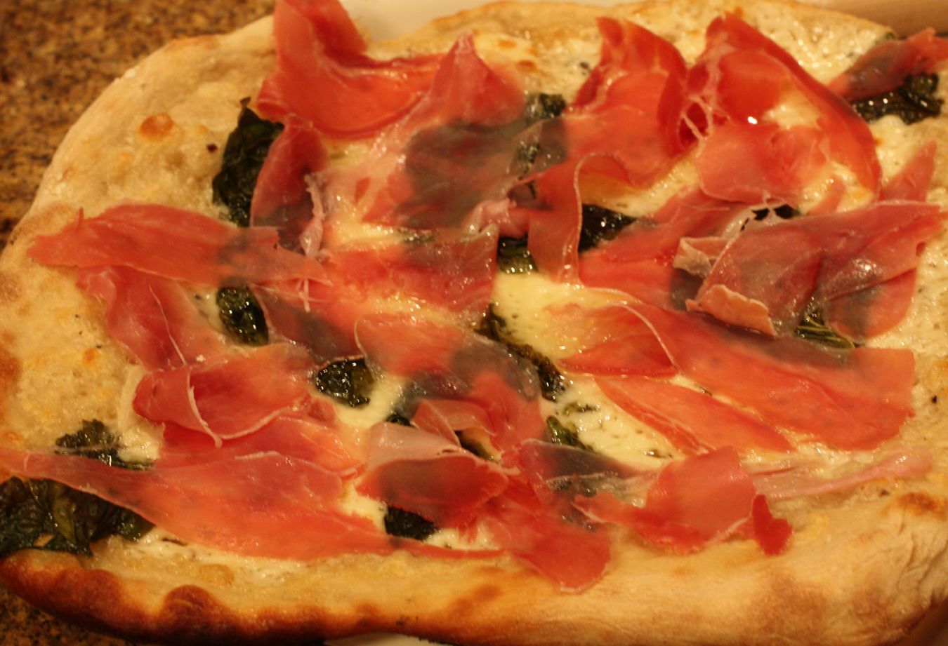 Pizza topped with garlic, basil, truffle cheese, and prosciutto.