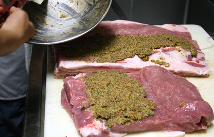 Center cut pork pork loin being smeared with a mixture of grainy mustard, anchovies, garlic, rosemary and thyme.