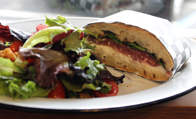 Half a prosciutto-burrata sandwich with salad.
