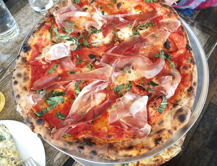 A Margherita gets draped with prosciutto. 
