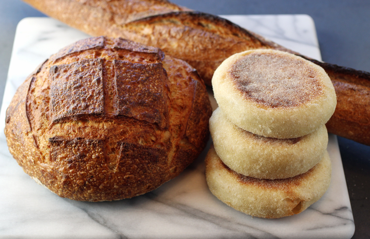 A baguette, a black pepper-Gruyere boule, and a stack of English muffins.