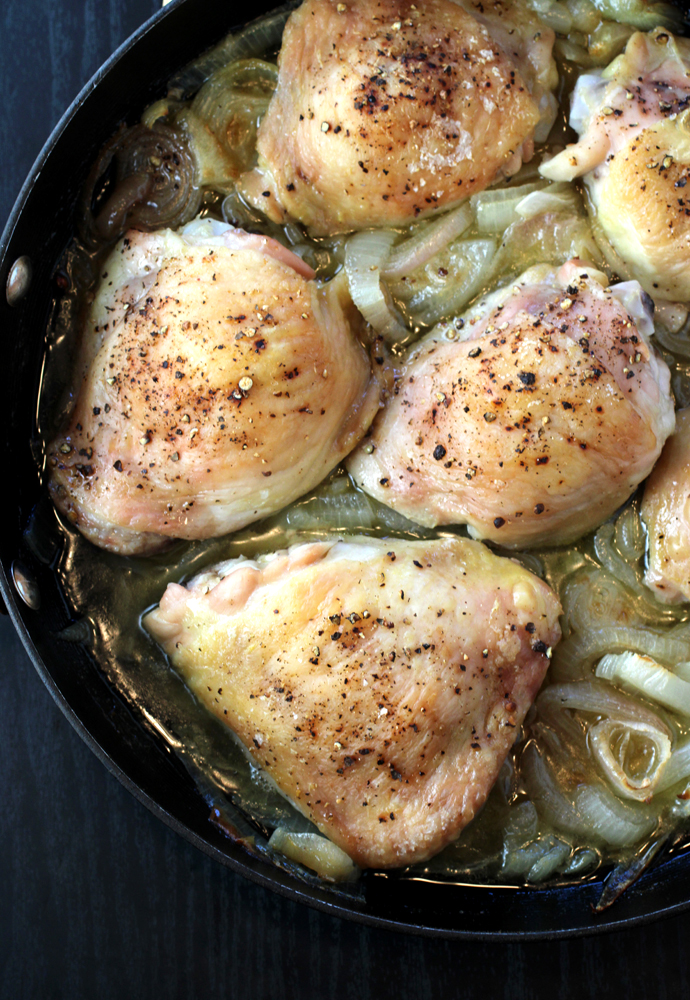 The chicken thighs cooked in a pan atop a bed of sliced onions and shallots.