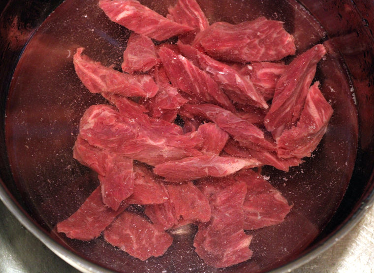Flank steak gets a soaking in a cool tub of water, before getting a vigorous deep-tissue massage.