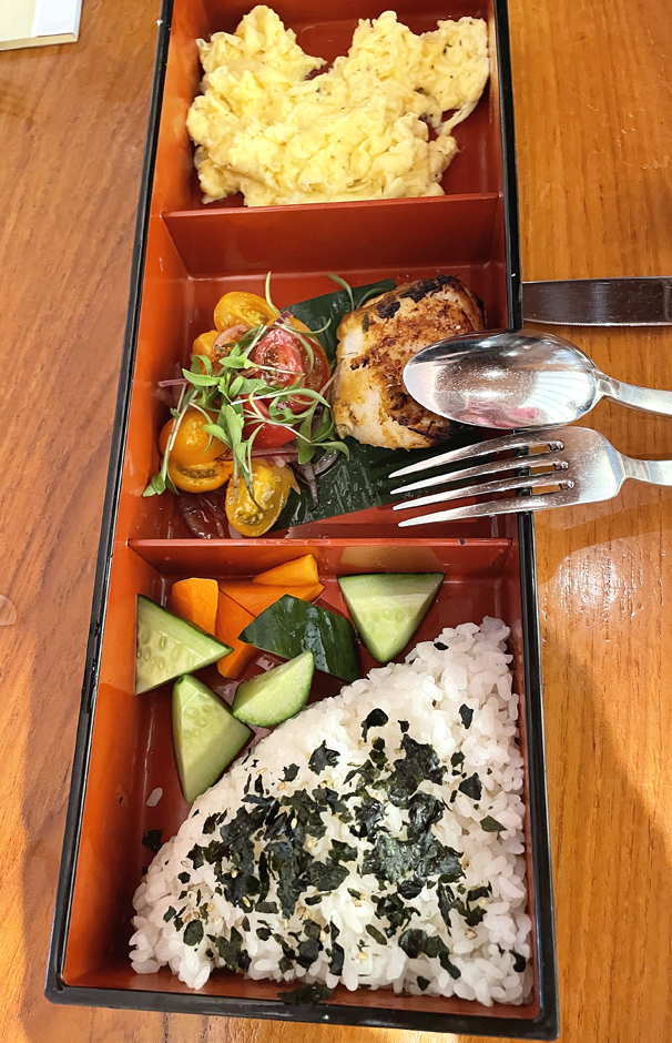 Japanese breakfast bento with truffle scrambled eggs, sea bass, rice, pickles, and miso soup.