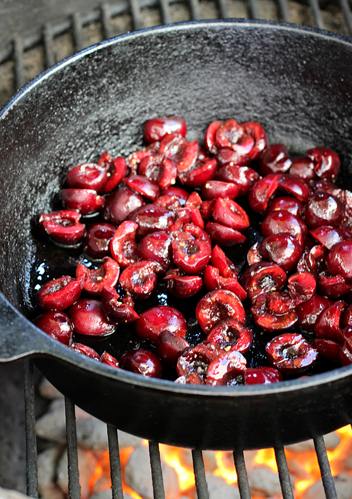 Pitted and halved cherries get grilled in a pan over the fire.