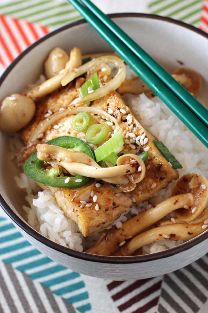 Slices of firm tofu get cooked in a sweet soy sauce with onions and mushrooms for comfort in a bowl.